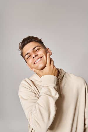 attractive man in his 20s with brown hair touching to jawline with hand on grey backgroundの写真素材