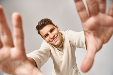 cheerful man with brown hair and grey eyes holding out his hands to camera against light background