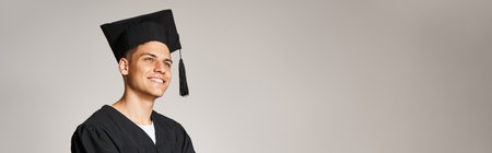 horizontal shot of attractive student in graduate gown and cap smiling and looking forwardの写真素材