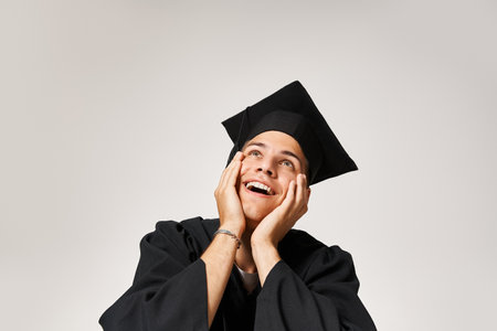 portrait of happy handsome man in graduate cap looking up in admiration on grey backgroundの写真素材