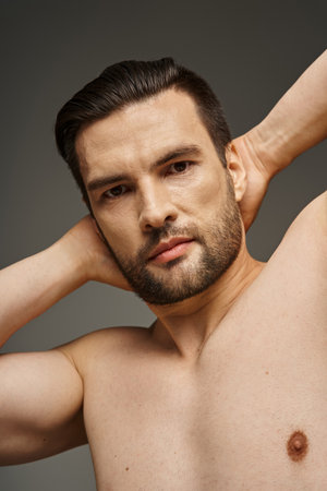 portrait of muscular and shirtless man with bare chest and bristle posing on grey backdrop