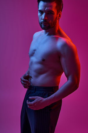 portrait of handsome man posing in pinstripe trousers on purple backdrop with red and blue lightsの写真素材