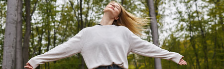 Peaceful and relaxed blonde woman dancing in forest jeans and sweater on backpacking trip, banner