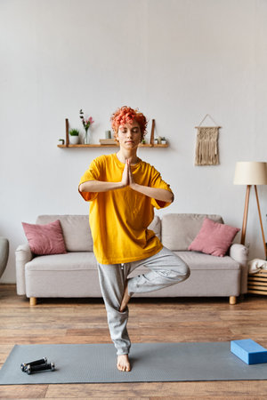 attractive red haired queer person in vivid outfit meditating with closed eyes while at homeの写真素材