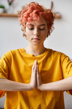 appealing young queer person in vivid yellow t shirt sitting on mat and doing some yoga at homeの写真素材
