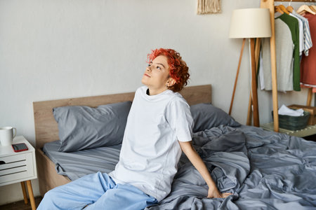 good looking extravagant person in white t shirt with red hair sitting on her bed, leisure timeの写真素材