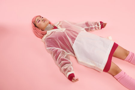 asian woman in 20s with silver necklace, pink hair and makeup lying down on vibrant backgroundの写真素材