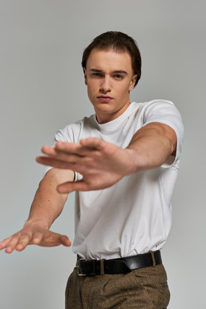 handsome polished young man in stylish clothing posing on gray background and looking at cameraの写真素材
