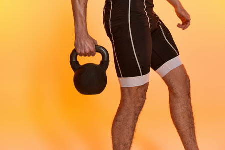 cropped view of young athletic man posing topless and exercising with kettlebell on orange backdropの写真素材