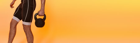 cropped view of young man posing topless while exercising with kettlebell on orange backdrop, bannerの写真素材