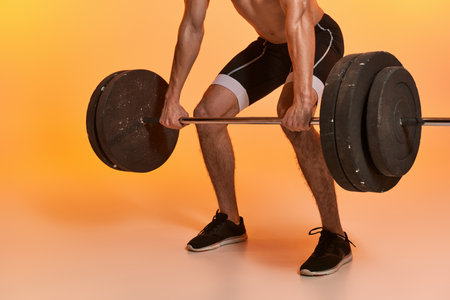 cropped view of young sporty man posing shirtless exercising with barbell on vibrant backgroundの写真素材