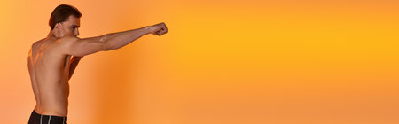 alluring shirtless sexy man in black shorts boxing actively on vibrant orange background, bannerの写真素材