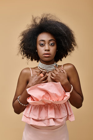 pretty dark skinned woman with curly hair posing in peach color ruffled top on beige backgroundの写真素材