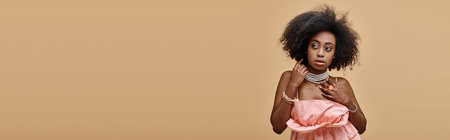 banner of pretty dark skinned woman with curly hair posing in peach ruffled top on beige backgroundの写真素材