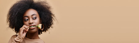 curly african american woman with small rose in teeth on beige background, peach fuzz bannerの写真素材