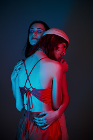 young lgbt couple with bold makeup and stylish attire hugging under purple lights in studio