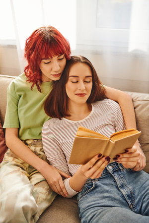 pleased lgbt couple enjoying quiet moment of reading together, wrapped in love and comfortの写真素材