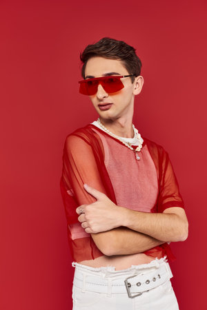 sophisticated androgynous man with red stylish fishnet and sunglasses posing and looking awayの写真素材