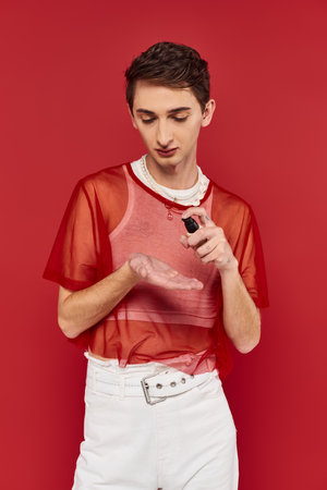 attractive and stylish androgynous man holding makeup foundation or concealer on red backdropの写真素材