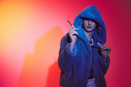 alluring androgynous man in purple stylish faux fur using mascara while on vibrant backgroundの写真素材