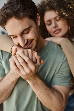 Warm morning hug of a smiling curly young woman and brunette man, holding hands in love