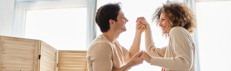 Lovely young couple spending time together at home dancing holding hands with smile, banner