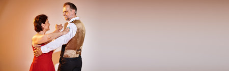 Ballroom dance mature couple in red dress and suit dancing tango with yellow light on grey, bannerの写真素材