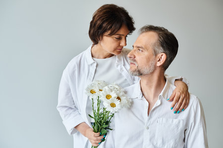 Portrait of happy mature couple with flowers on grey background, woman hugging and leaning on manの写真素材