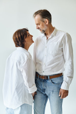 Portrait of happy mature couple standing together on grey background and smiling to each otherの写真素材