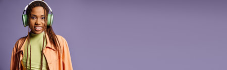 happy african american woman in vibrant attire with wireless headphones on purple backdrop, bannerの写真素材