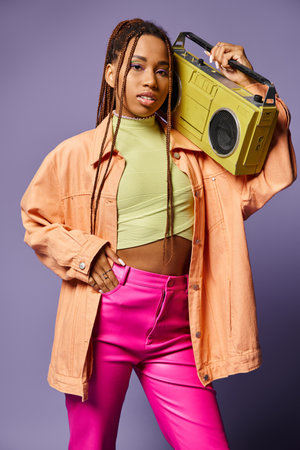 stylish african american girl with dreadlocks standing with retro boombox on purple backdrop