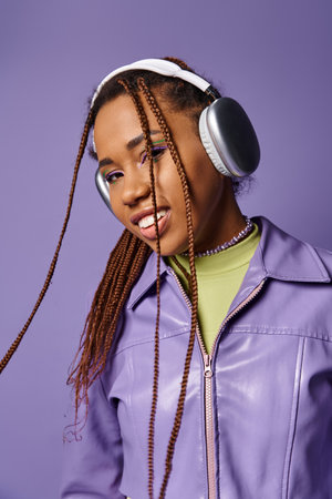 Smiling young african american woman with wireless headphones enjoying music on purple backgroundの写真素材