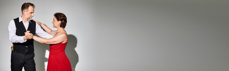 Portrait of mature attractive couple in red dress and suit dancing on grey background, bannerの写真素材