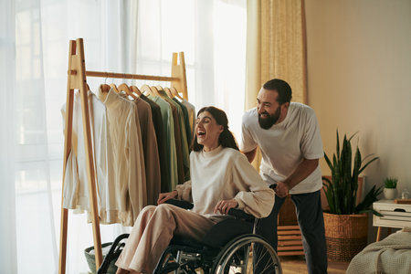 handsome caring man helping his inclusive wife on wheelchair to get dressed while in bedroomの写真素材