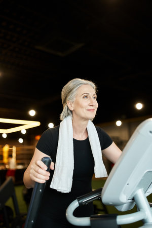 attractive cheerful senior sportswoman in black t shirt exercising actively on elliptical trainer