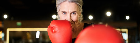 happy senior woman in sportswear with boxing gloves training on ring and smiling at camera, bannerの写真素材