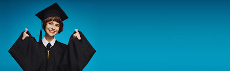 cheerful graduate college girl in academic cap making heart sign with her fingers on blue, bannerの写真素材