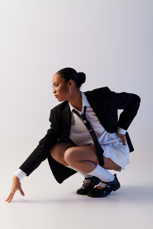 Young African American woman in a suit and tie kneeling down in a studio settingの写真素材