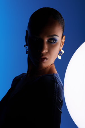 A young African American woman captivated by a white sphere in a studio setting.の写真素材