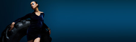 A young African American woman in a black dress holds a large black object in a studio setting, bannerの写真素材