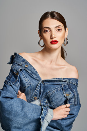 A young Caucasian woman with brunette hair wearing a trendy jean jacket and bold red lipstick.の写真素材