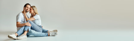 A couple, embodying romance and intimacy, sit closely together on the ground in a peaceful and...