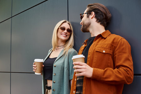 A glamorous man and woman stand closely together, holding coffee exuding romance and allure.