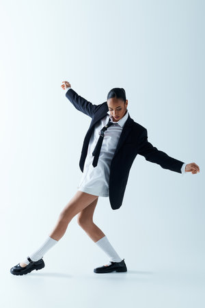 A young black woman in a stylish suit and tie joyfully dancing in a studio.