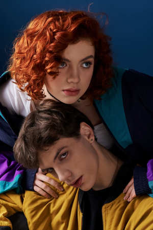 appealing red haired woman hugging her young boyfriend in vibrant attire who looking at cameraの写真素材