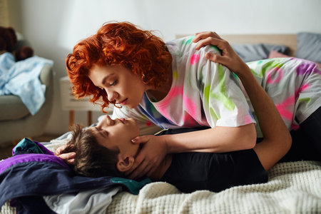 delighted young couple in comfy homewear preparing to kiss seductively while lying on bed together