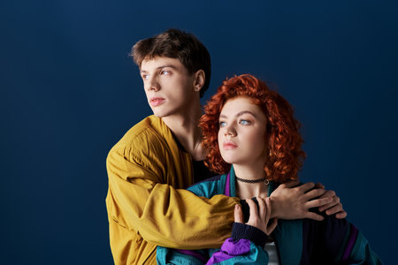 beautiful woman and her boyfriend in vibrant clothes hugging and looking away on blue backdrop