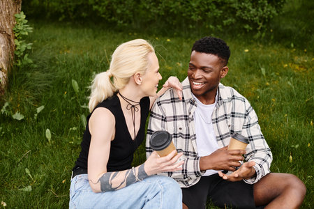 A happy multicultural couple, an African American man and a Caucasian woman, sitting together on the grass in a park.の写真素材