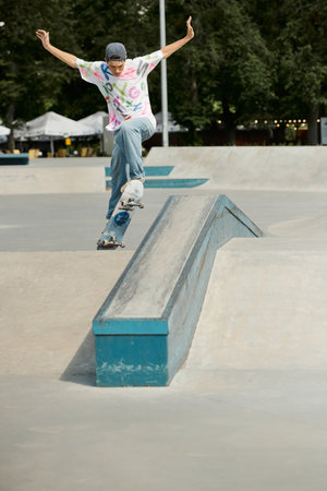 A young skater boy rides his skateboard up the steep side of a ramp in a vibrant outdoor skate park on a sunny summer day.の写真素材