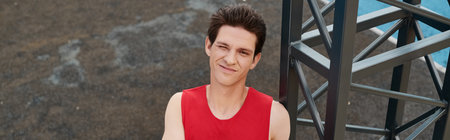 A young man in a red shirt stands next to a metal structure on a sunny day, showcasing a connection...